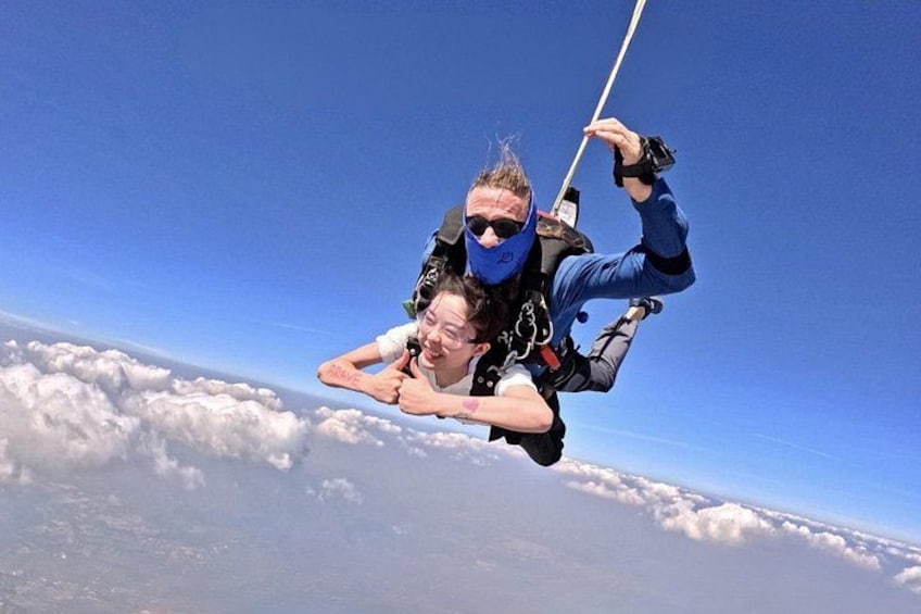 Two individuals skydiving above clouds with a clear blue sky. 2