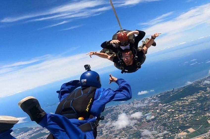 A person skydiving with a parachute, another person in a blue jumpsuit, and a landscape with buildings below. 1