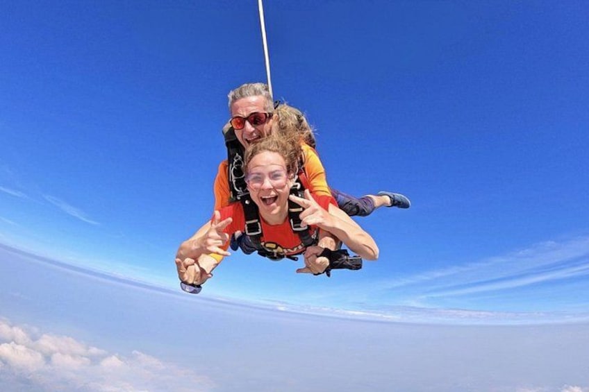 Two people skydiving with a clear blue sky and clouds below. 5