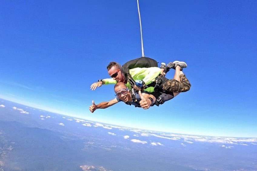 Two people skydiving with a clear blue sky and clouds below. 4