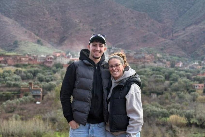 Twee personen staan in een bergachtig gebied, met een dorpje op de achtergrond. 1