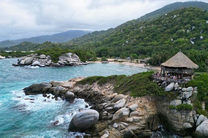 Un paisaje costero con grandes rocas, una playa y una estructura con techo de paja. 3