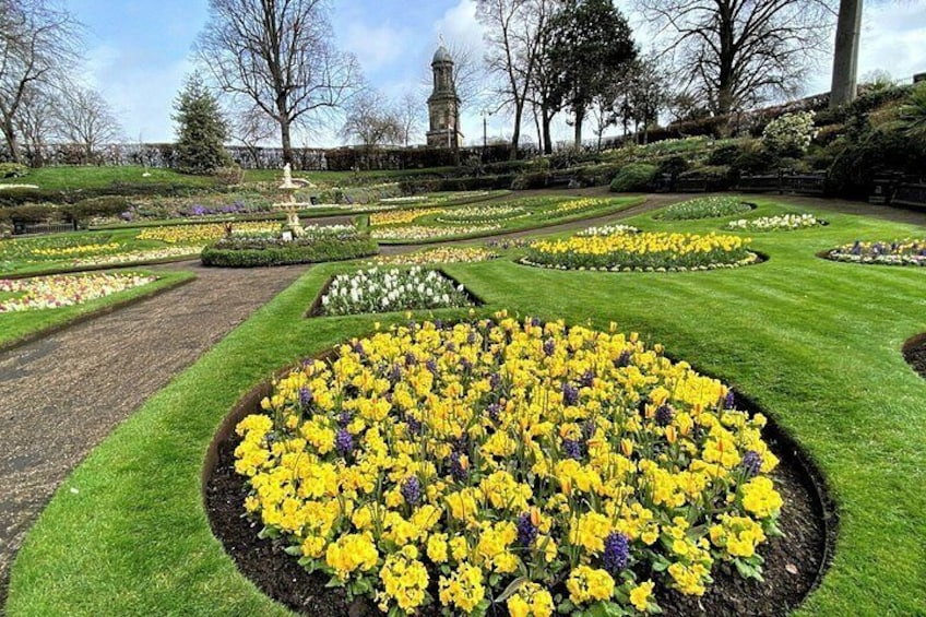 A formal garden with circular flower beds, a central fountain, and a distant tower. 5