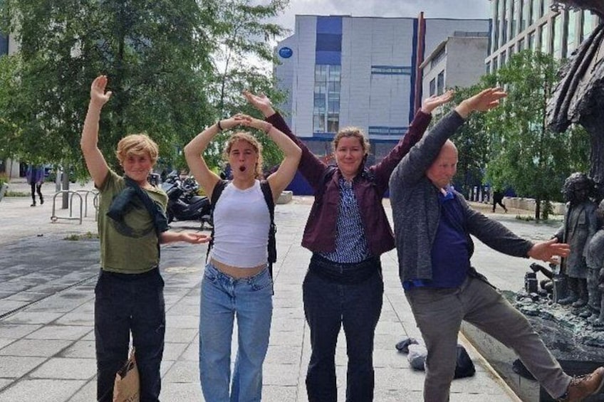 Four people posing with their arms raised in an outdoor urban setting with trees and buildings in the background. 3