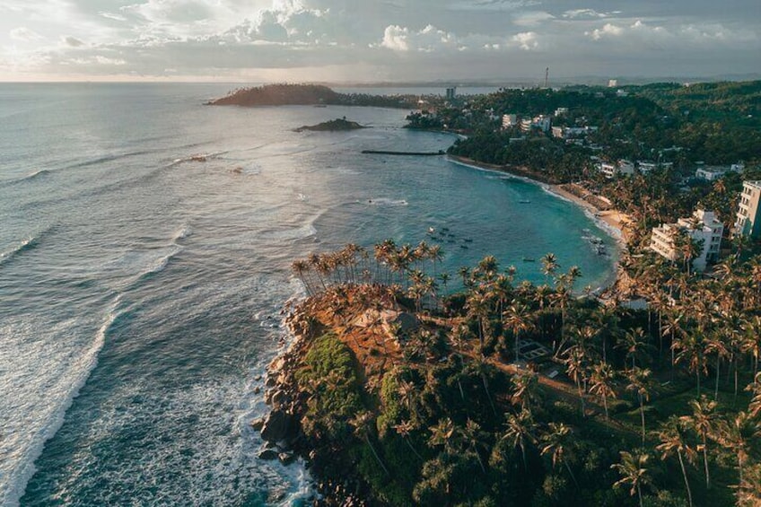 A coastal landscape with a beach, palm trees, and buildings along the shore. 3