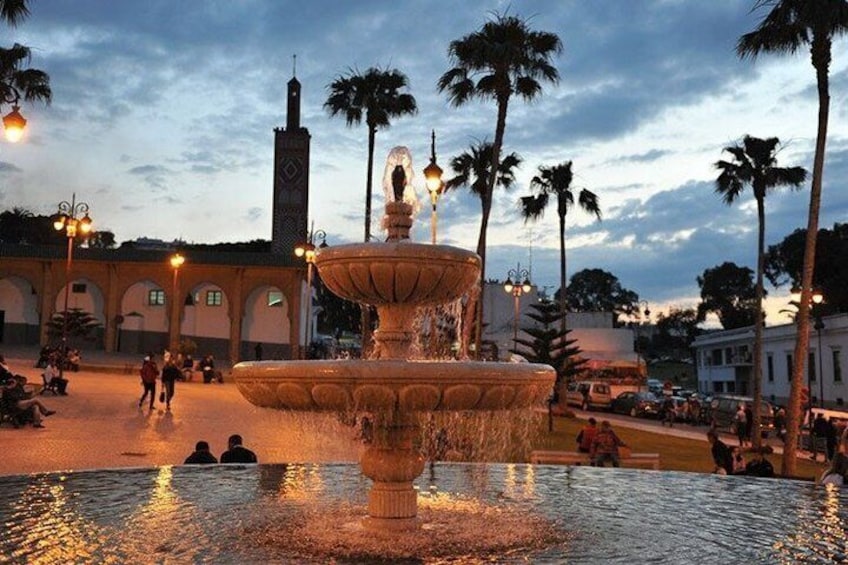 Une fontaine avec des jets d’eau, des palmiers et une mosquée dont le minaret se détache à l’arrière-plan. 3