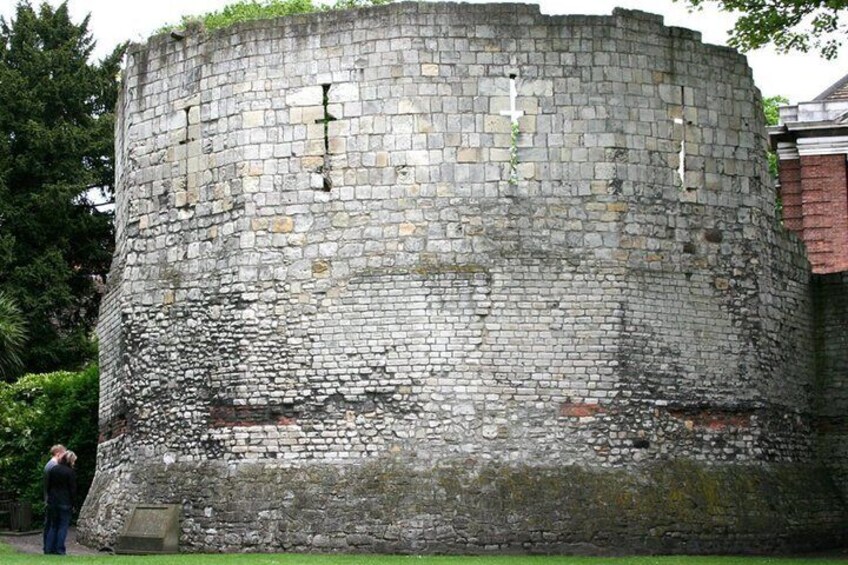 A historic stone wall with a circular structure, possibly a fortification, surrounded by greenery. 2