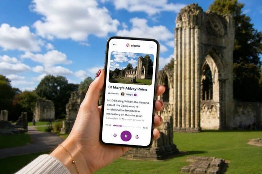 A hand holding a smartphone displaying St Mary's Abbey Ruins with a historic stone structure in the background. 1