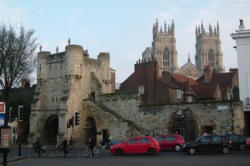 A historic stone castle with a large archway, a red car, and a black car parked in front. 5