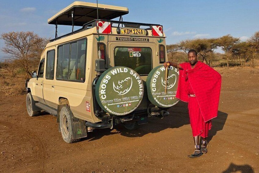 A safari vehicle with two spare tires and a person in traditional attire standing beside it. 3