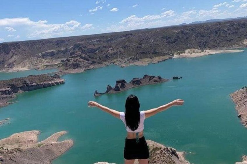 A person standing on a cliff overlooking a large body of water with rocky terrain in the background. 2