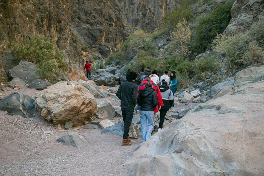 A group of hikers navigating a rocky trail with large boulders and sparse vegetation. 4