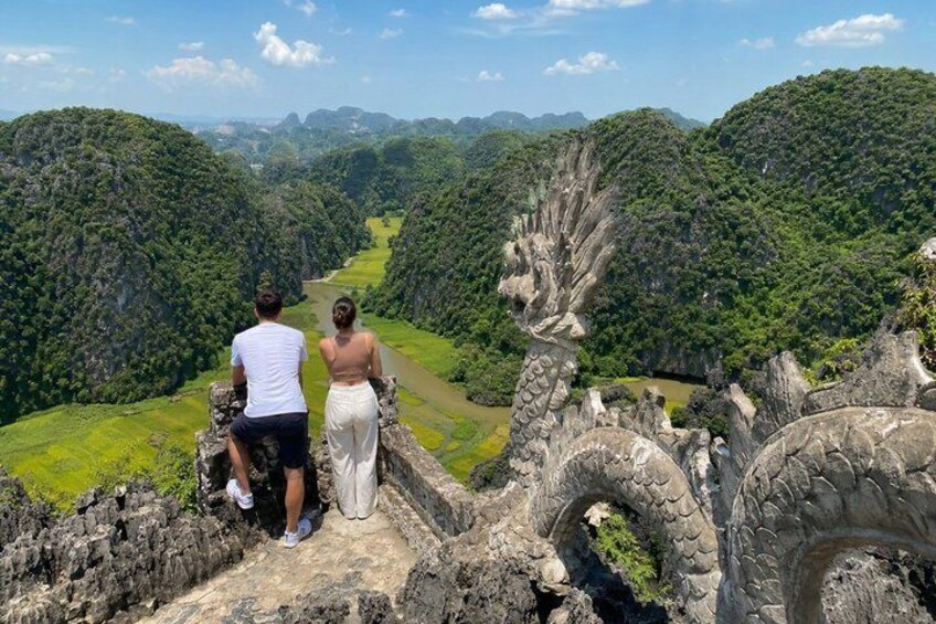 A couple overlooking a lush valley with a river and a stone bridge. 1