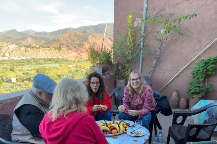 Un gruppo di persone sedute a un tavolo all'aperto con vista panoramica su montagne e vegetazione sullo sfondo. 2
