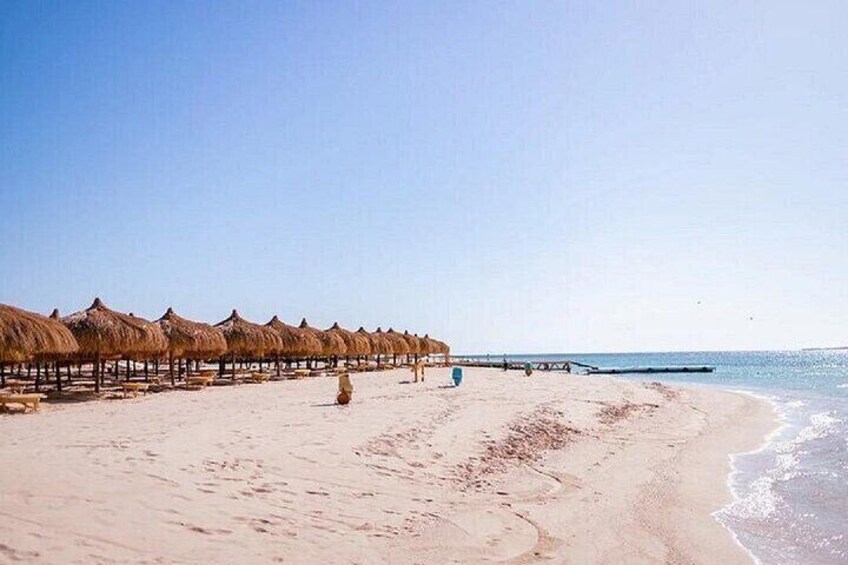 Una playa con sombrillas de paja y un muelle de madera que se adentra en el agua. 1