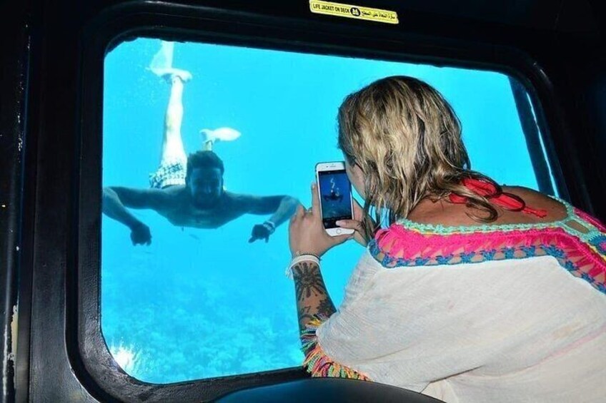 Una persona fotografiando una figura similar a una sirena bajo el agua, a través de una ventana. 5