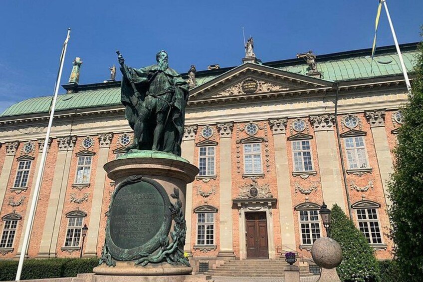 A large brick building with a statue in front, a green roof, and a flagpole. 3