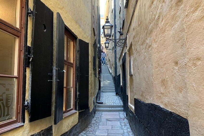 A narrow cobblestone alley with buildings on either side, closed shutters, and a street lamp. 5