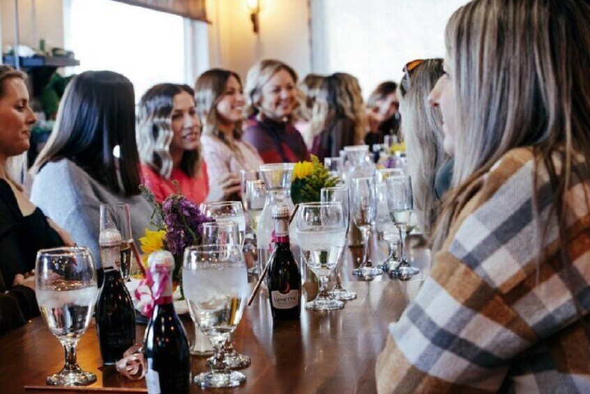 Un grupo de personas sentadas a una mesa con copas y botellas de vino. 1