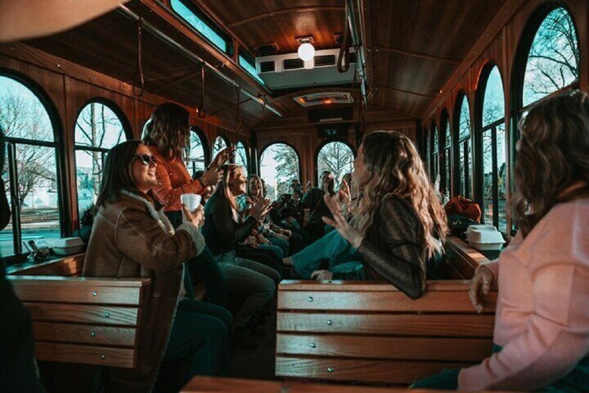 Un grupo de personas sentadas en bancos de madera dentro de un autobús con ventanas grandes. 3