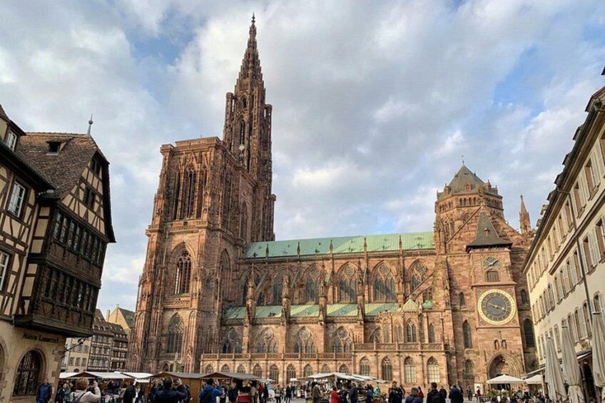 Une cathédrale historique, dotée d’une haute flèche, d’une grande horloge et bordée d’une place animée où se côtoient les passants et les étals du marché. 1
