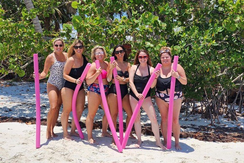 A group of people on a sandy beach holding pink sticks. 2