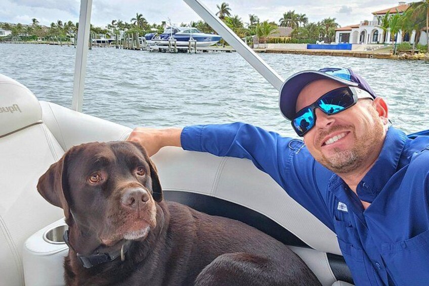 A man in a blue shirt and sunglasses on a boat with a dog. 5