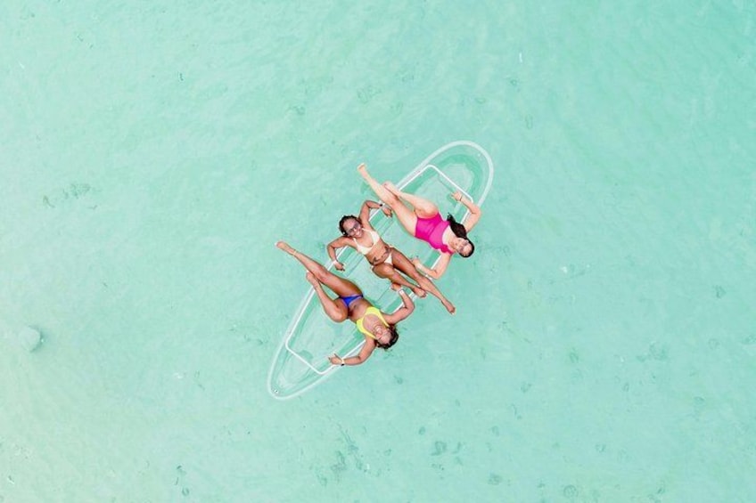 An aerial view of three people lying on a transparent inflatable raft in clear turquoise water. 2
