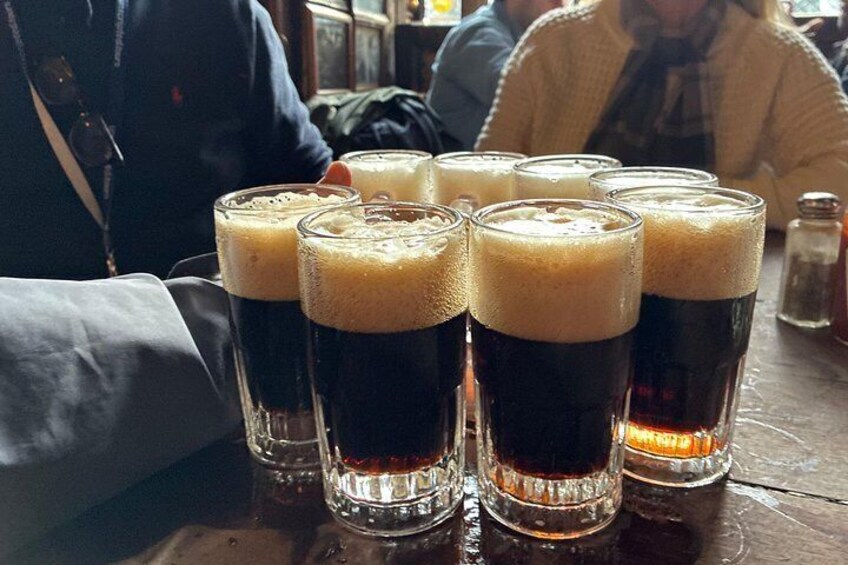 A table with several glasses of dark beer, some with foam on top. 5