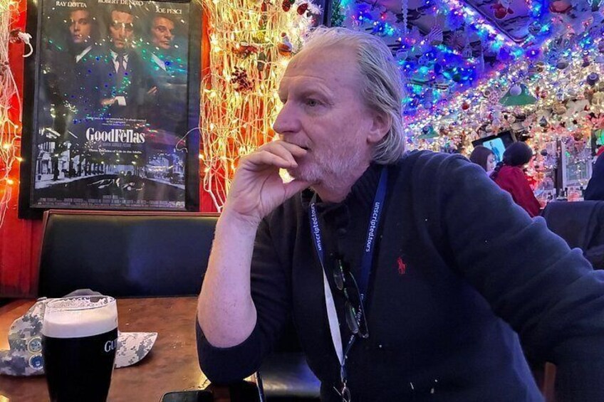 A person sitting at a table with a drink and a poster in the background. 2