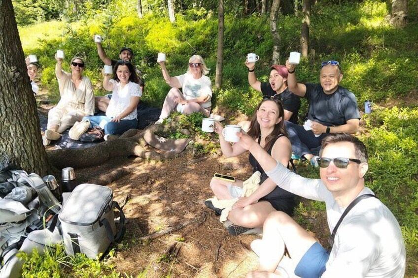 Un grupo de personas sentadas sobre un tronco en un bosque, sosteniendo tazas. 2