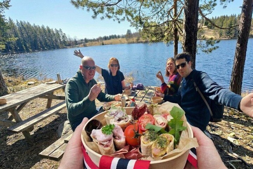 Un grupo de personas disfrutando de un picnic junto a un lago, con una mesa de madera y comida. 3