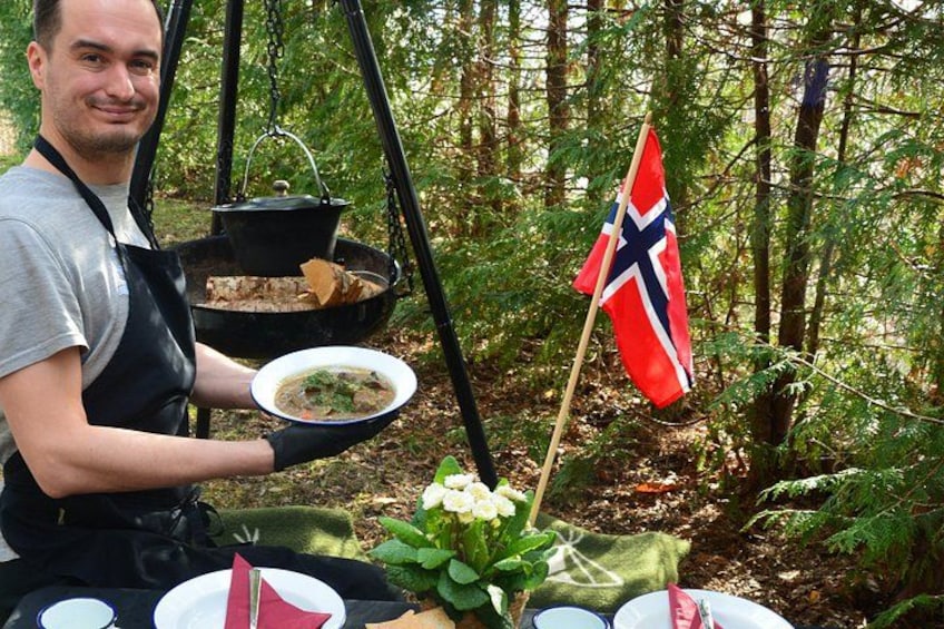 A person holding a plate of food outdoors with a flag and a pot on a stand. 2