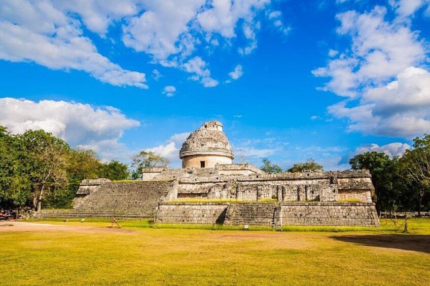 A large ancient pyramid with a dome structure, surrounded by a grassy area and trees. 5