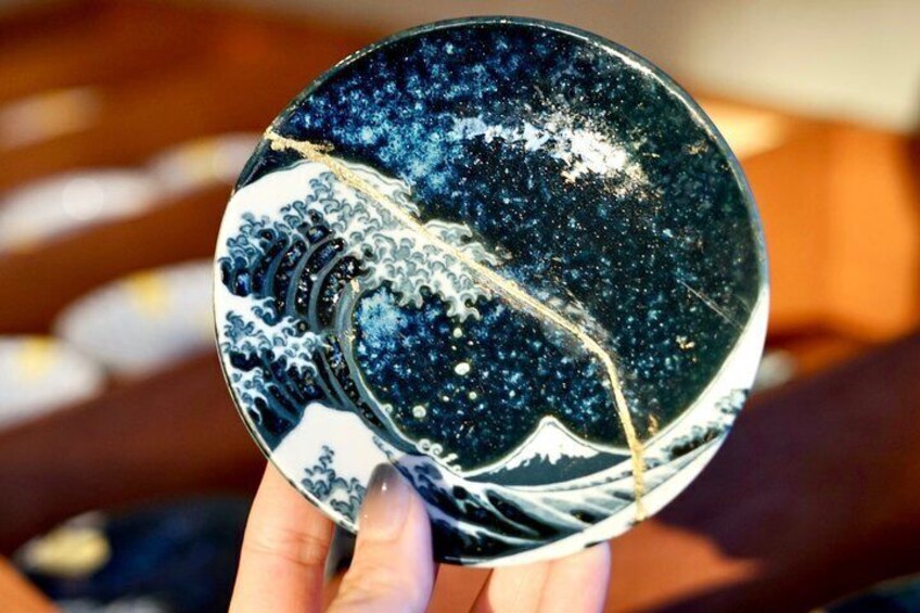 A hand holding a round plate with a wave pattern. 1