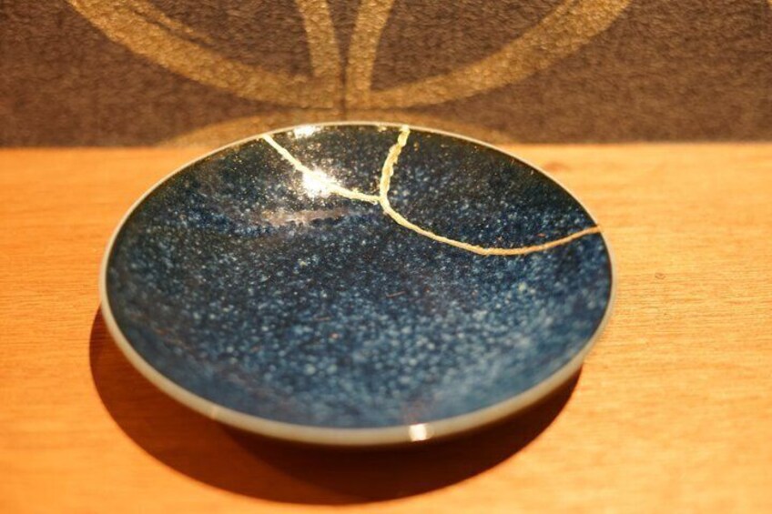 A round ceramic bowl with a crack on the rim, placed on a wooden surface. 2