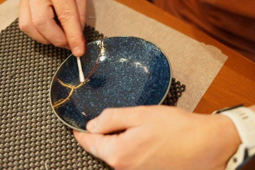 A person using a tool on a blue ceramic bowl. 5
