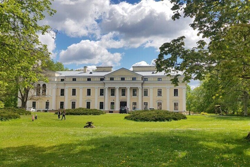 A large, classical building with a symmetrical facade, surrounded by a well-maintained lawn and trees. 1
