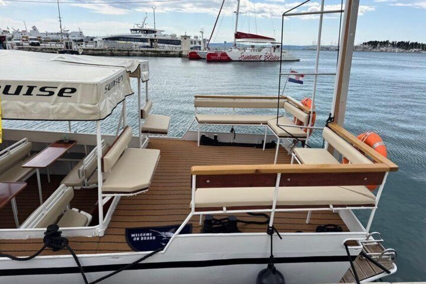 Un pont de bateau équipé de chaises longues, d’un espace abrité et d’un panneau indiquant : « Bienvenue à bord ». 2