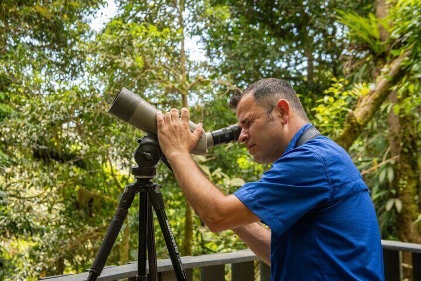 A man using a telescope on a tripod in a forested area. 3