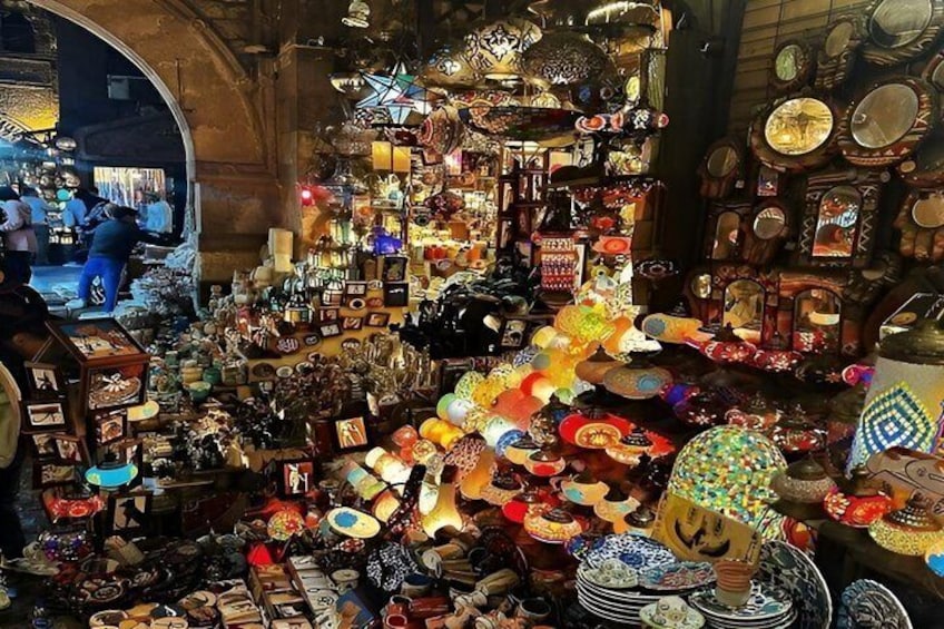 A crowded market with various stalls selling ceramics, textiles, and other goods. 2