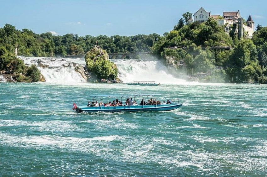 A boat with passengers on a river with a waterfall and a castle in the background. 2
