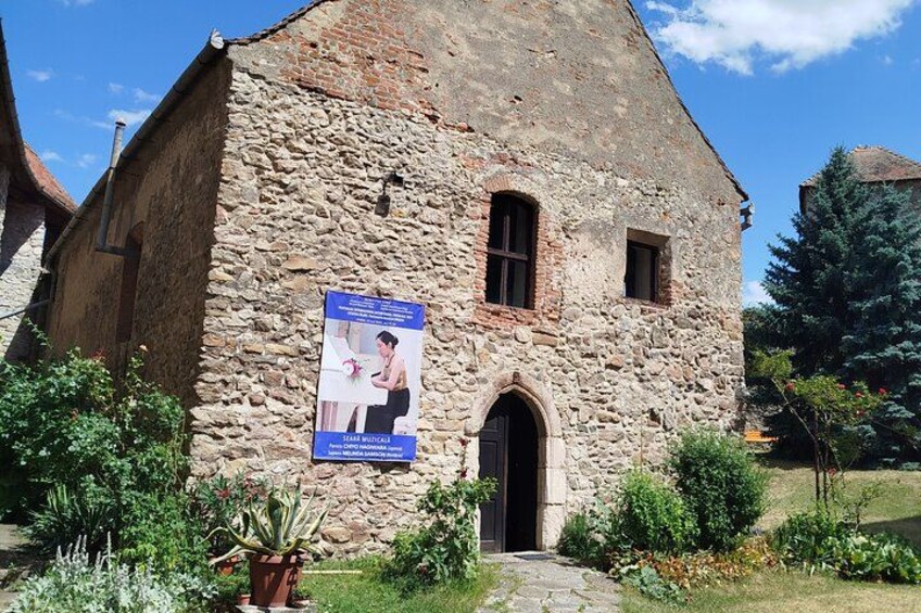 A stone building with a poster, a door, and a small garden. 5