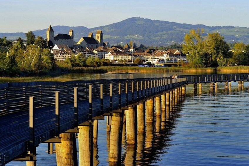 A wooden pier extending into a calm river, with buildings and a castle in the background. 2