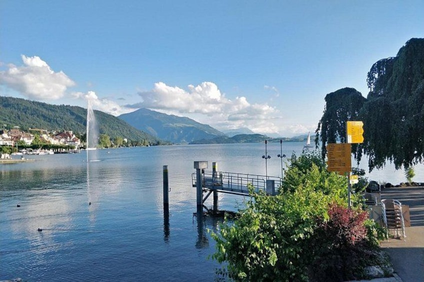 A lake with a fountain, a dock, and mountains in the background. 5