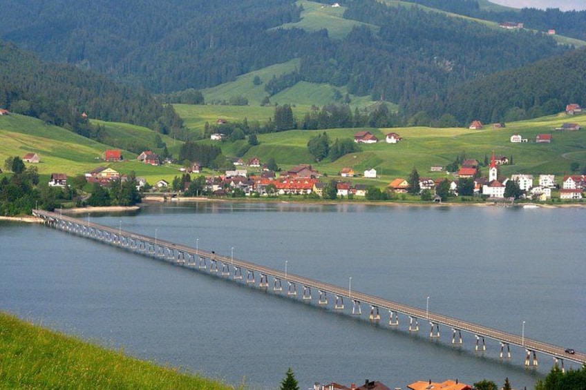 A long bridge over a lake with houses and greenery in the background. 3