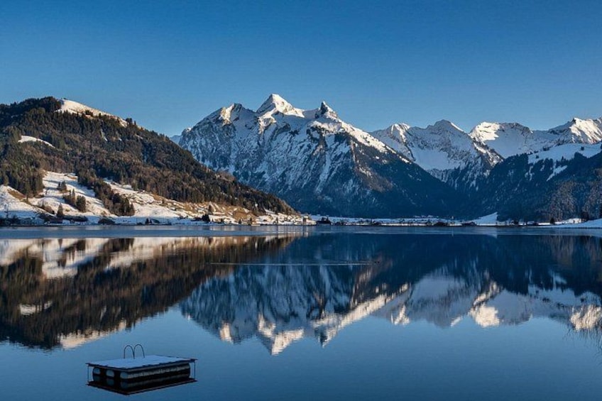 A calm lake reflecting snow-capped mountains, a clear sky, and a small boat in the foreground. 4