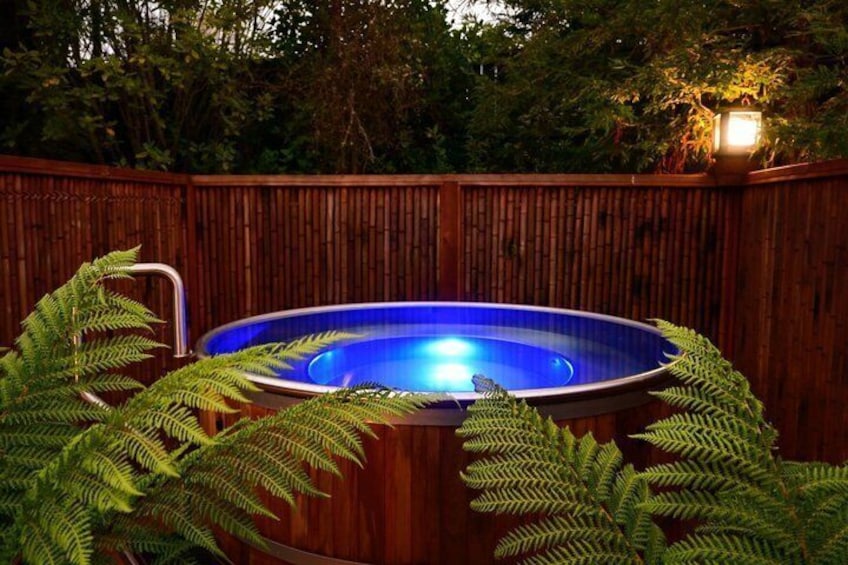 A hot tub surrounded by ferns, with a wooden fence and a lit lamp post in the background. 5