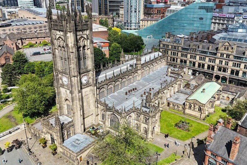 A historic church with a tall clock tower, surrounded by modern buildings and a green park. 2