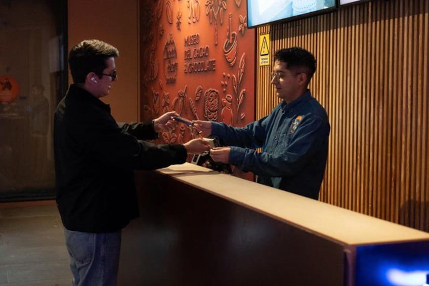 Dos hombres estrechan la mano en la recepción, con un panel de madera y un letrero de advertencia al fondo. 2